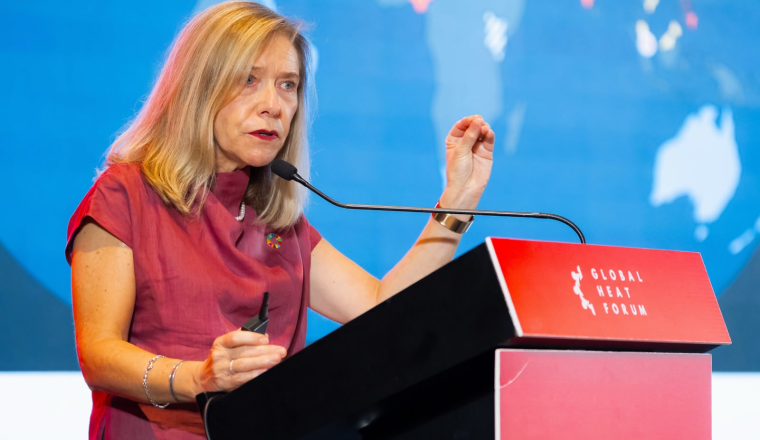A woman speaking at a podium labeled “Global Heat Forum” with a world map in the background.