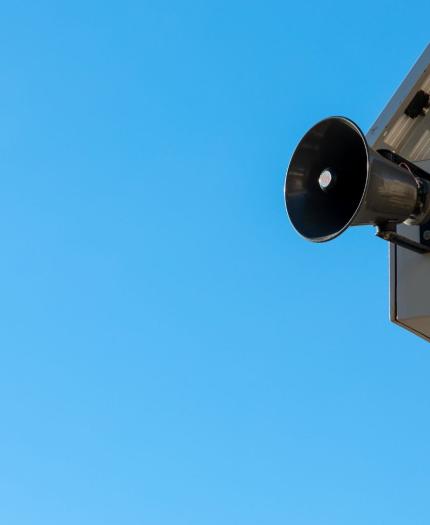 A loudspeaker attached to a pole is set against a clear blue sky.